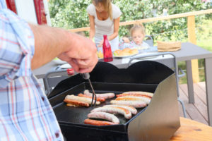 Familie grillt Bratwürste auf einer Grillplatte